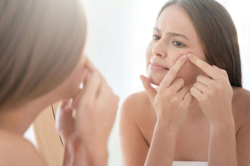 Jeune femme essayant de percer un grain de milium bouton blanc visage