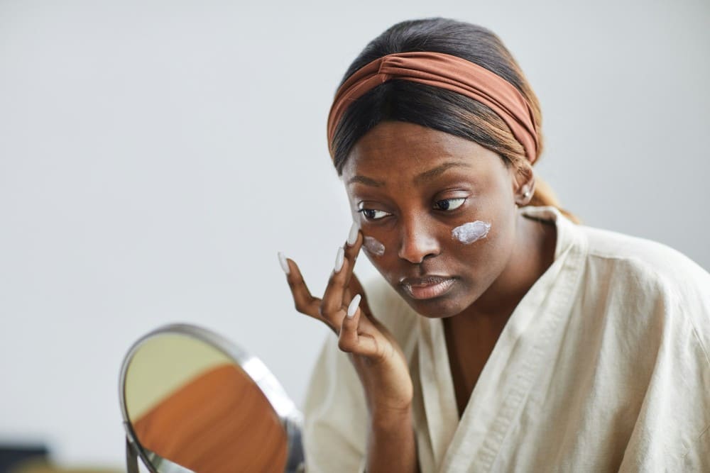 Femme de couleur noire mettant de la crème solaire tous les matins visage