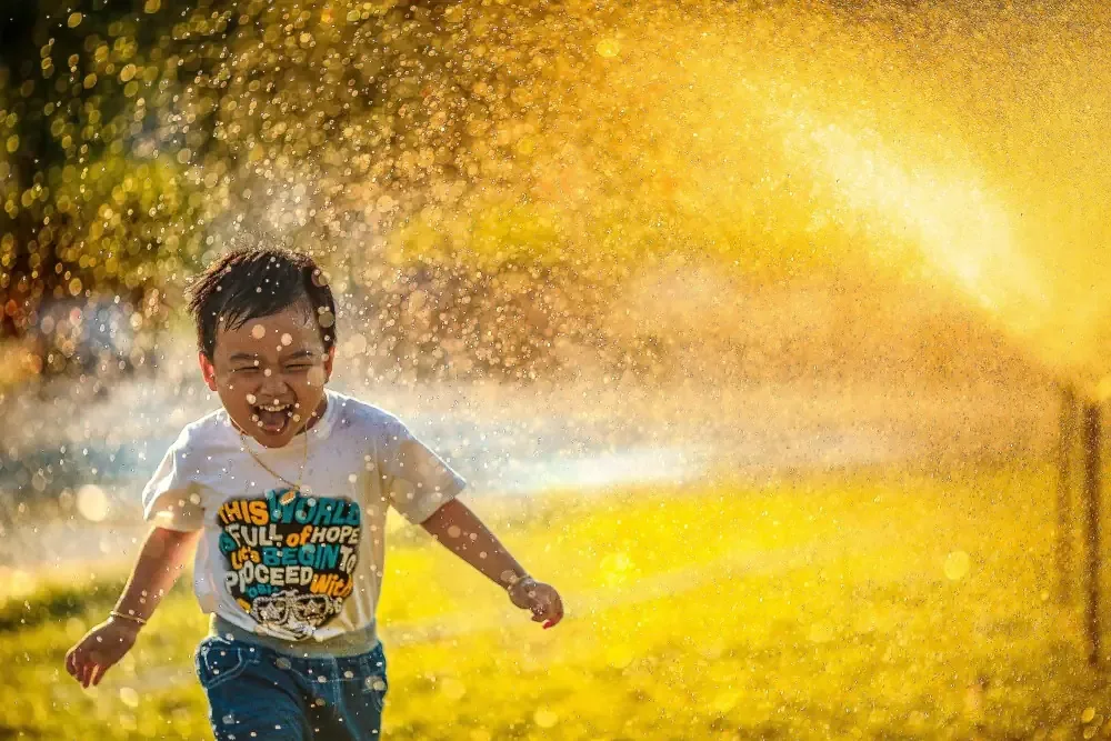 Enfant qui court sous un jet d'eau pour échapper à la vague de chaleur estivale