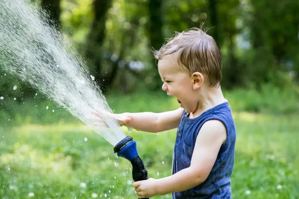 Jeune enfant qui a chaud et qui joue avec un jet d'eau pour se rafraîchir