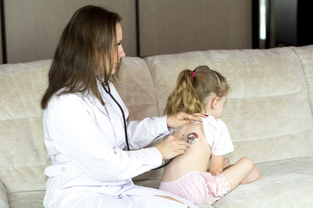 Médecin femme qui ausculte une petite fille sur son canapé