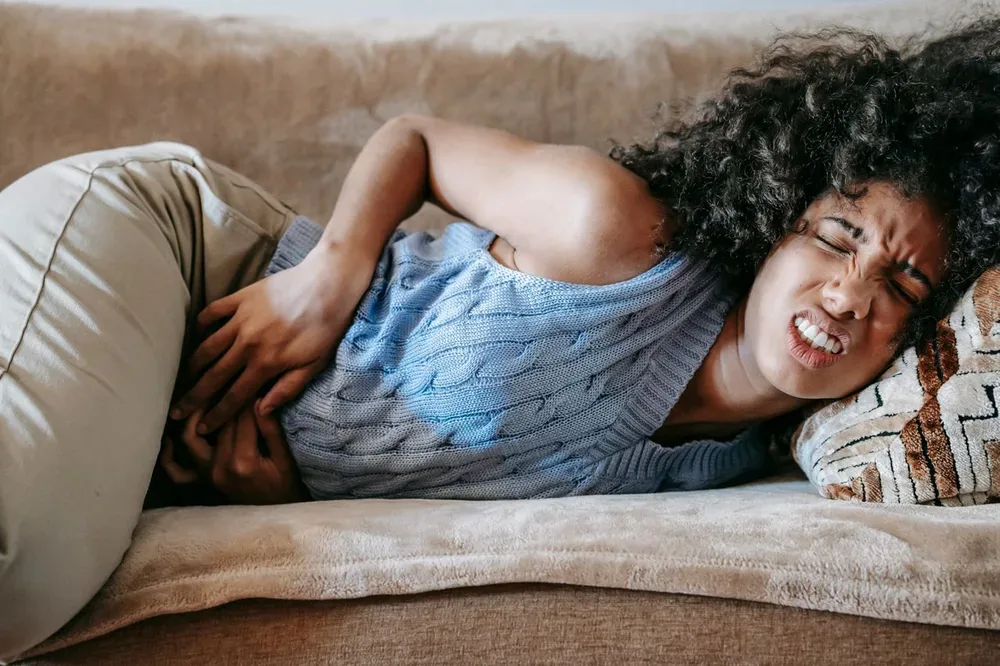 Femme allongée sur un canapé, main posée sur le bas-ventre à cause d'une douleur abdominale.