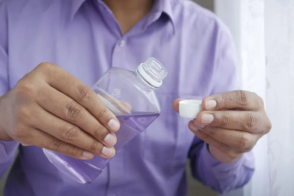 Personne en chemise violette versant du bain de bouche dans un bouchon doseur
