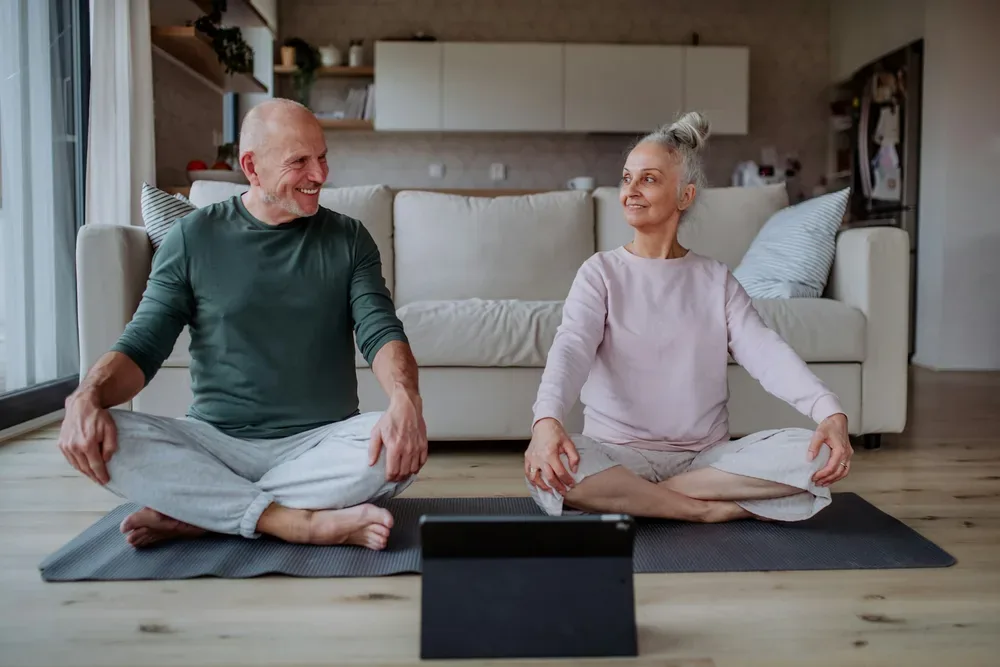 Un couple de personnes agees faisant des exercices de relaxation ensemble a la maison