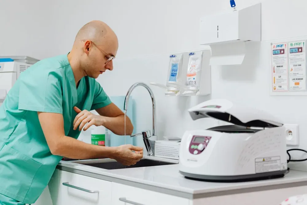 Professionnel de santé en tenue verte se lavant les mains au lavabo d'une salle de soins