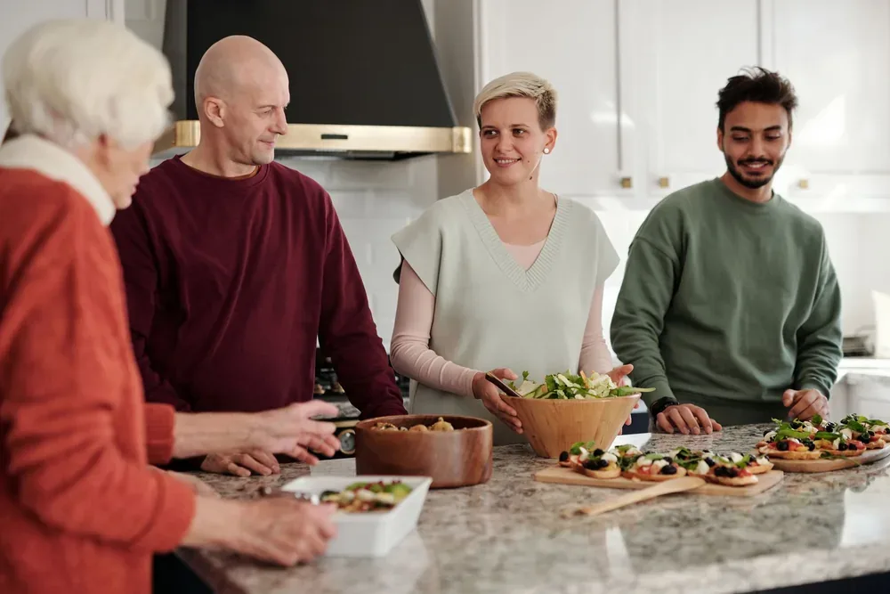 Quatre adultes discutent autour d'un plan de travail préparant des bruschettas et salades