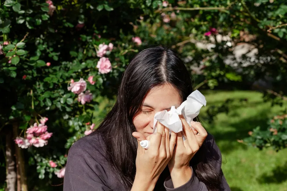 Éternuements : une femme se mouche avec un mouchoir dans un jardin fleuri.