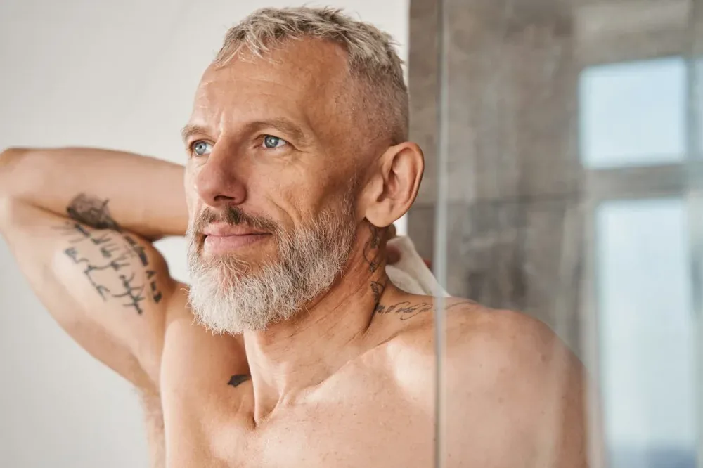 Homme torse nu barbu levant un bras, avec des tatouages visibles sur le bras et le cou
